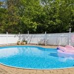 A round pool with a pink flamingo float and a white fence surrounding it.