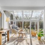 A room with large glass front, wooden table, armchairs and plants.