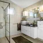 Bathroom with shower, sink and toilet. White cabinets, mirror and tiles.