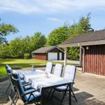 Terrace with table and chairs beside a wooden house. Lawn and trees in the background.