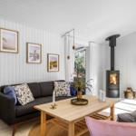 Living room with sofa, coffee table, and wood stove. Walls with pictures and plants.