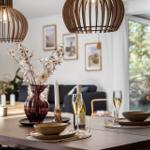 Dining table with wine, glasses, and vase under wooden lanterns.