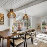 Dining area with table and chairs, view into living room with sofa and windows.