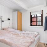 Schlafzimmer mit Bett, Kleiderhaken und Fenster. Wandverkleidung und Holzboden.