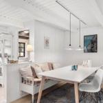 Essbereich mit Tisch, Stühlen und Sofa. Weiße Wände und Decke. Küchenbereich im Hintergrund.