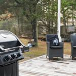 Gartenbereich mit Grill und zwei Sitzgelegenheiten auf Holzterrasse.