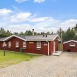 Rotes Holzhaus mit Garage und gepflastertem Hof im Wald.