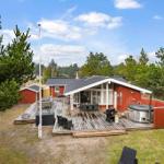 Rotes Ferienhaus mit Terrasse, Whirlpool und Grill unter Bäumen.