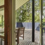 Terrasse mit Holztisch und Stühlen, umgeben von Wald und blauem Zaun.