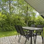 Terrasse mit Tisch und Stühlen, umgeben von grüner Vegetation und einem Holzdeck.