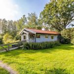 Ein kleines Haus mit rotem Dach steht auf einer grünen Wiese umgeben von Bäumen.