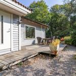 Haus mit Terrasse, Tisch und Stühlen, umgeben von Bäumen und Pflanzen.