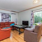 Wohnzimmer mit rotem Sofa, braunem Sessel und Holzboden. Fenster mit Blick auf Garten.