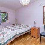 Schlafzimmer mit Bett, Nachttisch und Stuhl. Fenster mit Blick auf Grün.