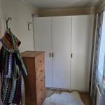 Schlafzimmer mit Kleiderschrank, Holzkommode und Fenster mit Vorhängen.