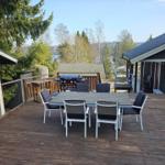 Holzterrasse mit Tisch, Stühlen und Grill. Blick auf Wald und Wasser.