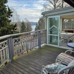 Terrasse mit Blick auf See und Bäume, mit Sitzgelegenheiten und Schiebetür.