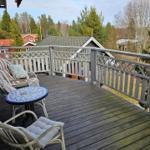 Terrasse mit Holzboden, Gartenmöbel und Blick auf Wald und Häuser.