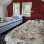 Zimmer mit zwei Betten, roten Wänden und zwei Fenstern mit Blick auf Wald.