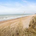 Strand mit Dünen und sanften Wellen im Hintergrund.