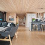 Living and kitchen area with wooden floor, ceiling, and walls. It has a sofa, chairs, and a kitchen island.