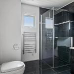 Bathroom with shower, toilet, and heater. Black tiles and window.