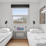 Two beds with white bedding, window with view of trees, wall shelf and wall art.