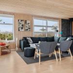 Living room with wooden walls, sofa, chairs, and TV. Large windows with view of green.