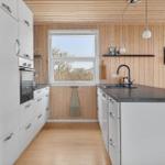 Kitchen with white cabinets, dark countertop, and wooden walls. Window with outdoor view.