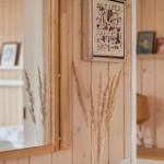 Mirror shows bedroom with wooden wall and pictures. Dried grass decorates the room.