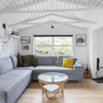 Ein Wohnzimmer mit grauem Sofa, runden Tisch und Kaminofen. Holzfußboden und weiße Wände.
