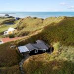 Schwarzes Haus mit Solaranlage auf Dünen, Blick auf Strand und Meer.
