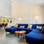Living room with blue sofa and wooden wall. Dining area with table and chairs in background.