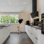 Modern kitchen with white countertop and wooden wall. Window with view of greenery.