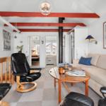 Living room with sofa, black chairs, and wooden table. Red beams on ceiling.