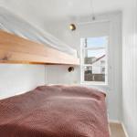 Room with double bed and window. White wall paneling. Wooden ceiling beams.
