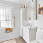Bathroom with shower, sink, and toilet. Window with curtain and wooden shelves.
