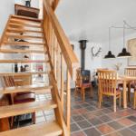 Wooden staircase leads to kitchen. Dining area with table, chairs, and stove.