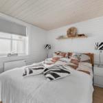 Schlafzimmer mit Bett, Nachttischen und Fenster. Wände und Decke sind weiß verkleidet.