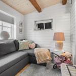 Ein Wohnzimmer mit grauem Sofa, weißen Wänden und Holzbalken an der Decke.