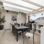 Terrasse mit Essbereich, Grill und Küchenzeile unter Dach.