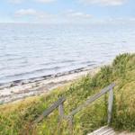 Holzsteg führt zu Strand und Meer. Gras und Blumen am Hang.
