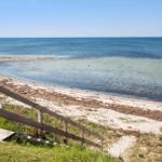 Holzsteg führt zum Strand mit klarem Wasser und Blick auf das Meer.