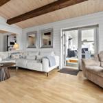 Wohnzimmer mit Sofa, Sessel und Holzboden. Deckenbalken und Glastür zur Terrasse.
