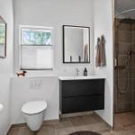 Badezimmer mit Dusche, Waschbecken und Toilette. Fenster mit Jalousie.