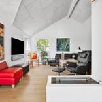 Wohnzimmer mit rotem Sitzmöbel, schwarzen Ledersofas und Fernseher an der Wand.