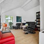 Wohnzimmer mit rotem Sofa, schwarzen Sesseln und Holzboden. An der Wand hängt ein großes Bild.