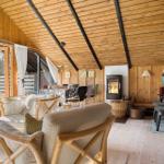 Wohn- und Essbereich mit Kamin, Holzwand und großem Fenster. Rattanmöbel und warmes Licht.