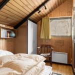 Schlafzimmer mit Holzwand, Bett, Stuhl und Fenster mit Vorhang.