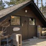 Hütte mit Holzfassade, Tür und Fenstern. Vor dem Haus steht ein Stuhl und eine Skulptur.